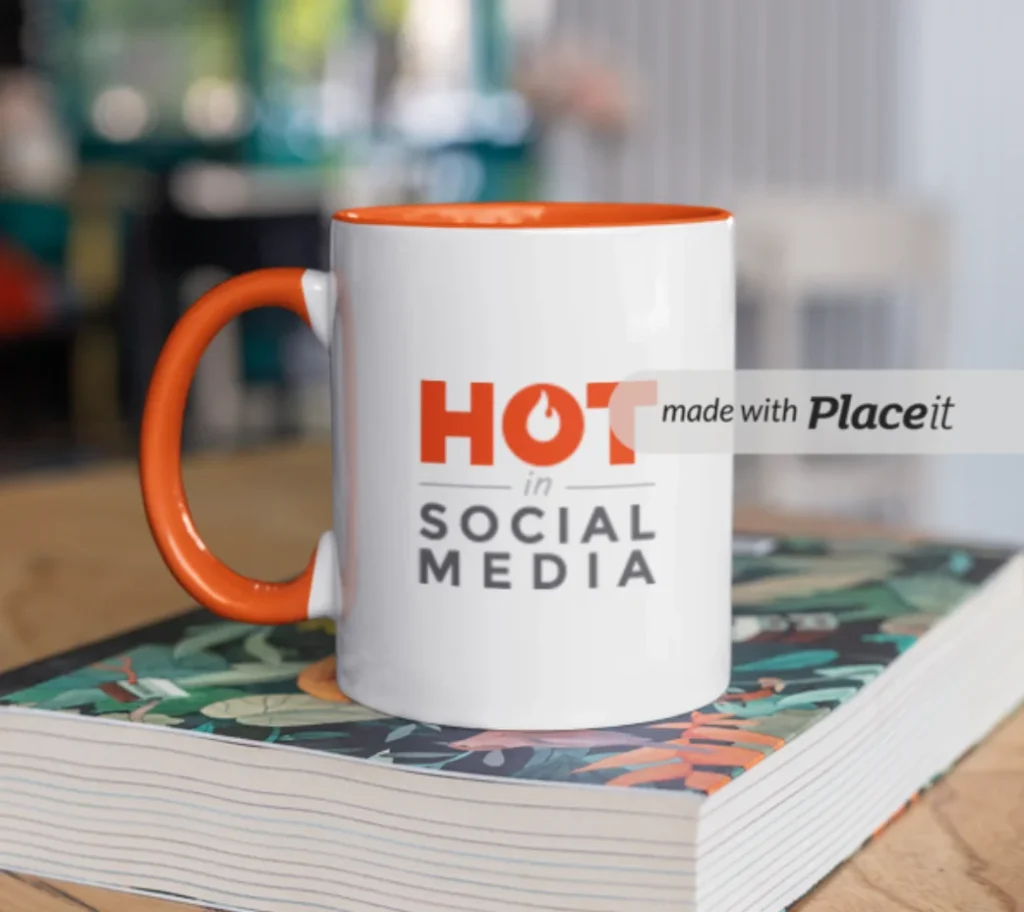 The Hot in Social Media logo on a mug that is sitting on a book on a wooden table.